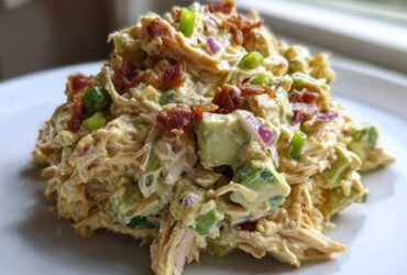 A mound of creamy honey mustard chicken salad mixed with chunks of avocado, red onion, and topped with crispy bacon bits.