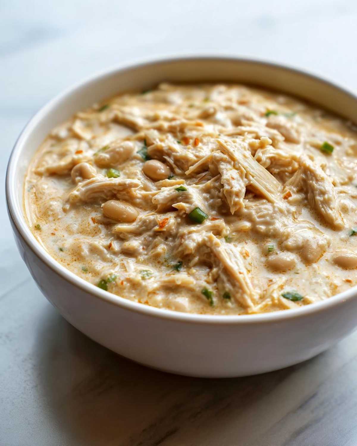 Close-up of creamy instant pot white chicken chili featuring shredded chicken and white beans in a white bowl.