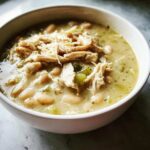 Close-up of a white bowl filled with creamy instant pot white chicken chili, topped with shredded chicken and white beans.