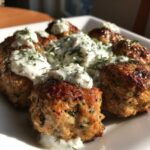 Close-up of browned greek chicken meatballs topped with creamy tzatziki sauce and fresh dill.