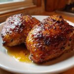 Two perfectly cooked, glistening honey garlic chicken thighs resting in sauce on a white plate.
