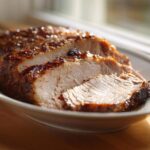 Close-up of sliced, juicy slow cooker turkey breast with a caramelized, dark glaze on a white platter.