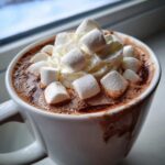 Close-up of a white mug filled with rich crockpot hot chocolate topped with whipped cream and marshmallows.