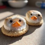 Two melted snowman cookies featuring toasted meringue tops, chocolate chip eyes, and orange candy noses on sugar cookies.