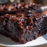 A close-up of a rich, dark slice of black bean brownies topped with melted chocolate chips on a white plate.