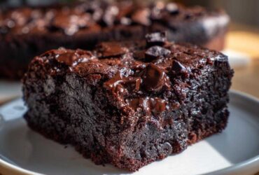 A close-up of a rich, dark slice of black bean brownies topped with melted chocolate chips on a white plate.