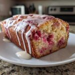 A slice of moist strawberry bread topped with a thick vanilla glaze, showing the bright red fruit baked inside.