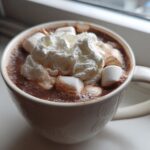 Close-up of a white mug filled with rich crockpot hot chocolate topped with marshmallows and whipped cream.