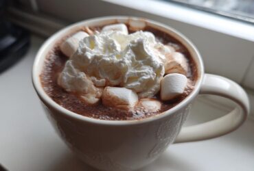 Close-up of a white mug filled with rich crockpot hot chocolate topped with marshmallows and whipped cream.