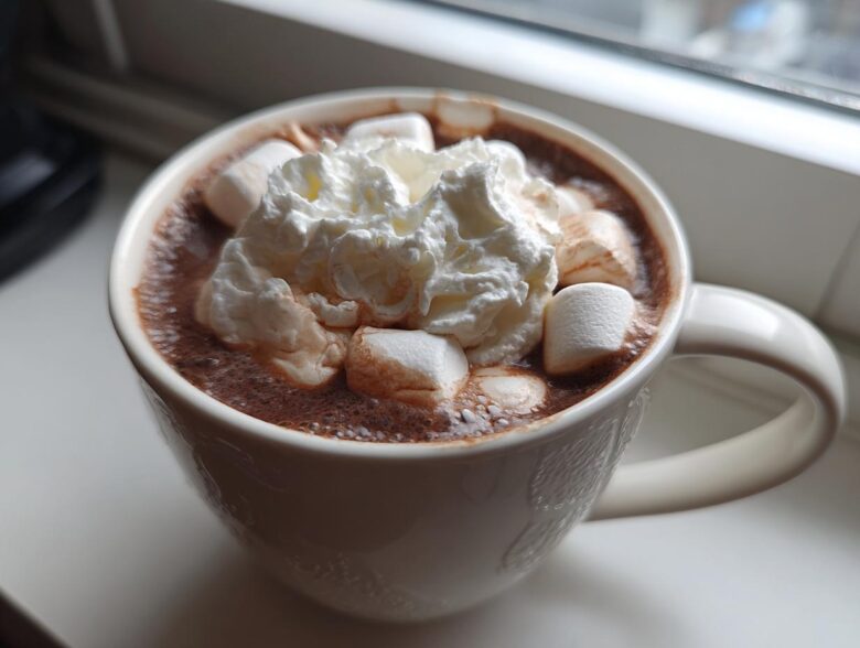Close-up of a white mug filled with rich crockpot hot chocolate topped with marshmallows and whipped cream.