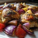 Close-up of crispy, herb-crusted greek chicken thighs served with roasted potatoes and red onions.