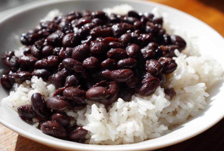 A close-up of a white bowl filled with fluffy white rice topped generously with saucy black beans, perfect for a beans and rice dinner.