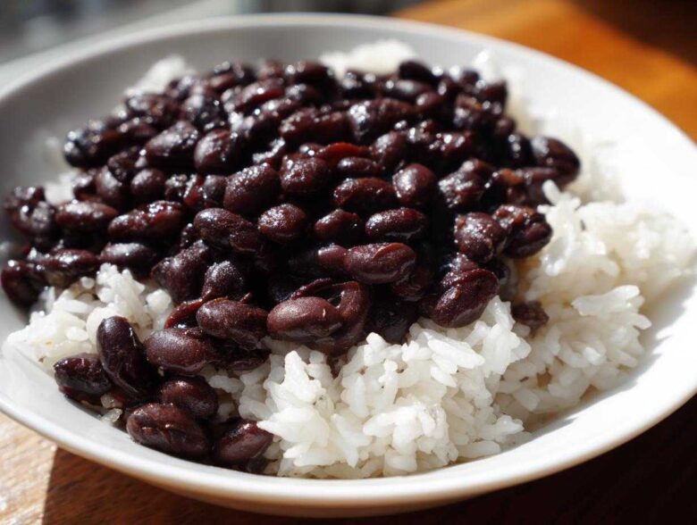 A close-up of a white bowl filled with fluffy white rice topped generously with saucy black beans, perfect for a beans and rice dinner.