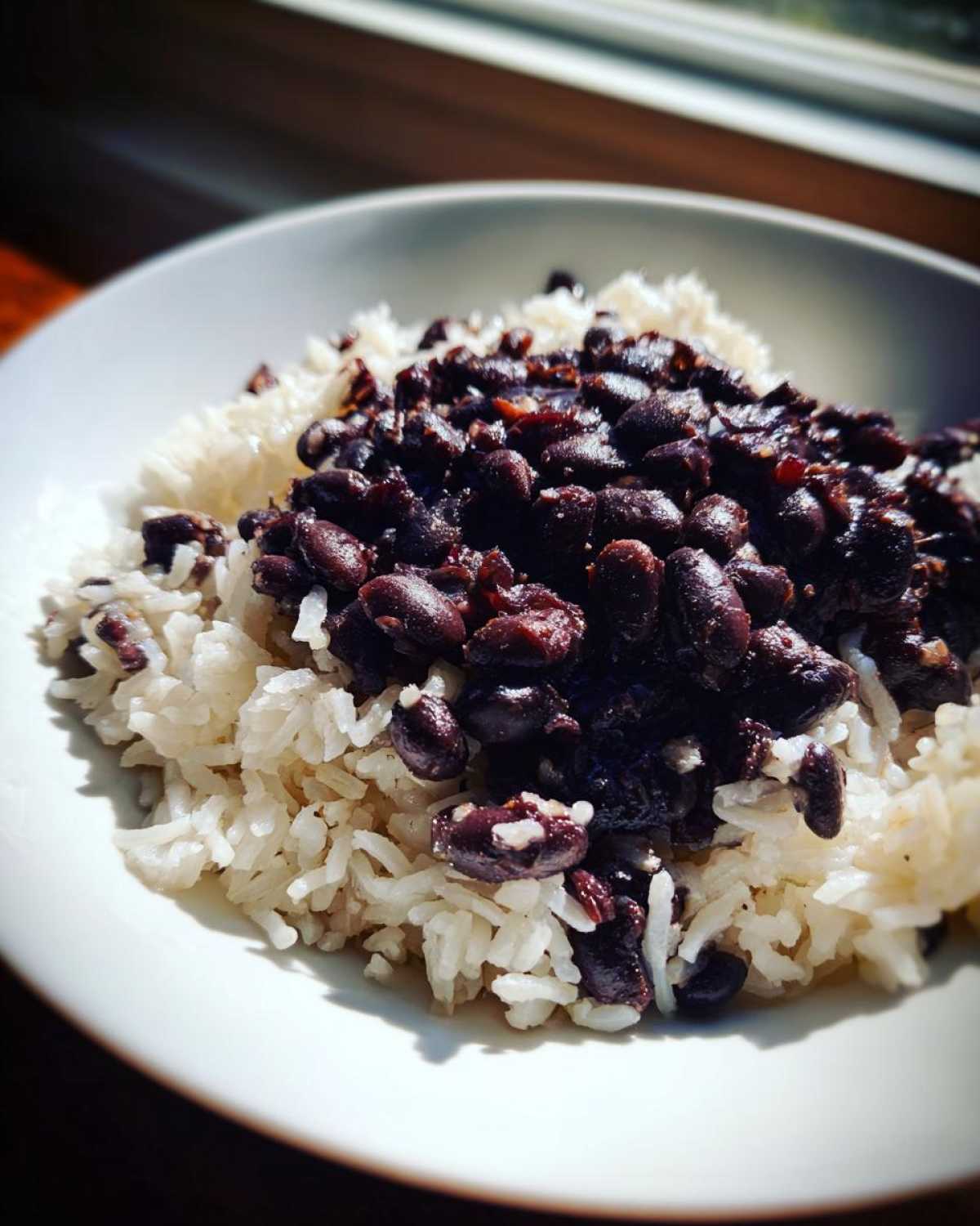 A close-up shot of fluffy white rice topped generously with dark, seasoned black beans, showcasing the simple beans and rice dish.