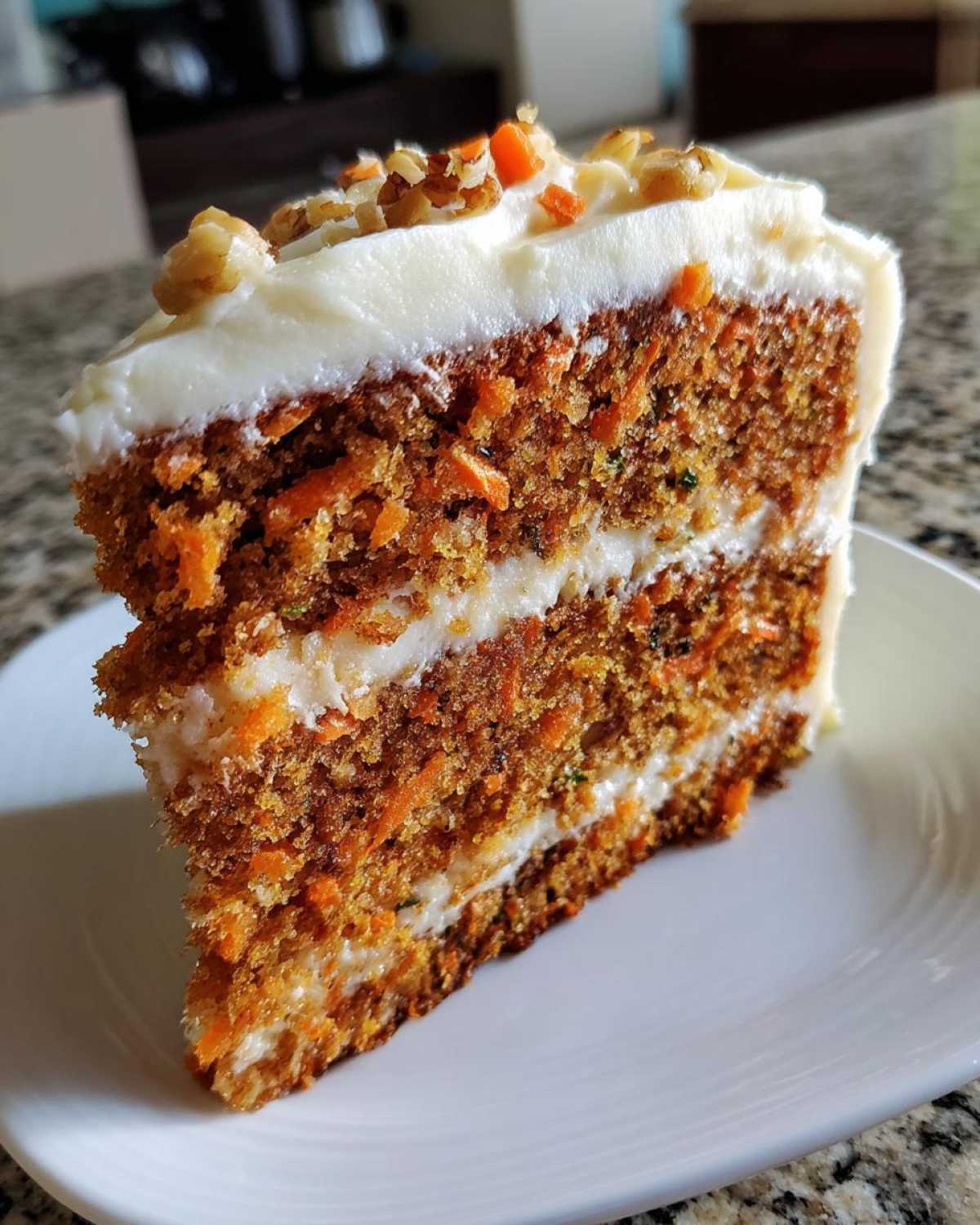 A thick slice of moist carrot cake recipe with two layers of cream cheese frosting, topped with walnuts.