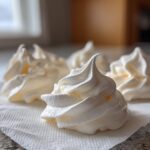 Close-up of four perfectly piped, white meringue cookies resting on a textured white paper towel.