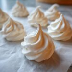 Close-up of perfectly piped, stiff-peak meringue cookies on parchment paper before baking.