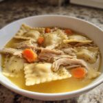 A bowl of quick chicken and dumpling soup featuring ravioli-style dumplings, shredded chicken, and sliced carrots in broth.