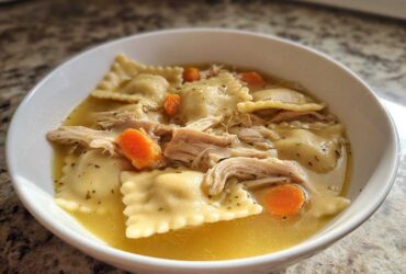 A bowl of quick chicken and dumpling soup featuring ravioli-style dumplings, shredded chicken, and sliced carrots in broth.