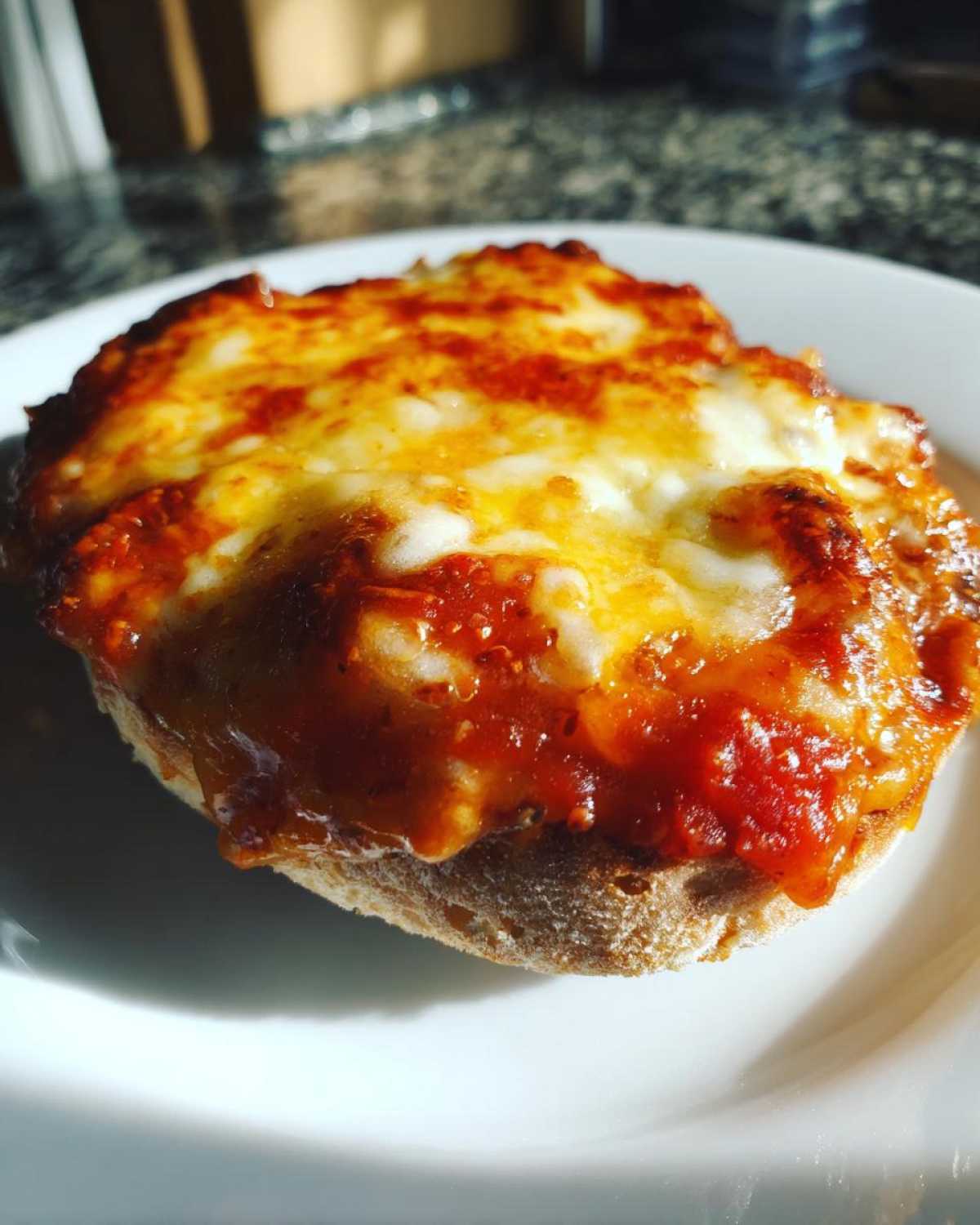 Close-up of a freshly baked english muffin pizza with bubbling, melted cheese and tomato sauce.