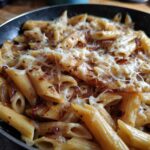 Close-up of penne pasta tossed with caramelized onions and melted cheese in a skillet, highlighting the french onion pasta.