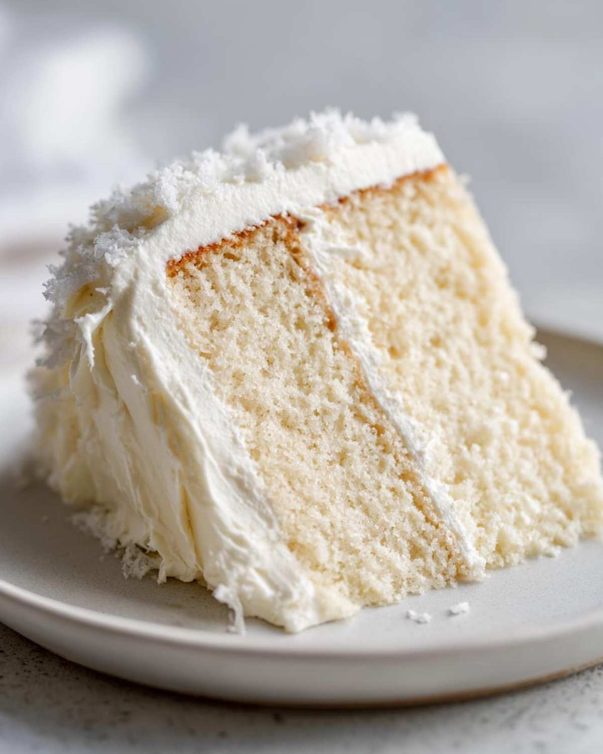 Close-up of a moist slice of white cake generously covered in fluffy vanilla buttercream frosting.