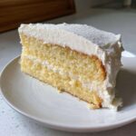 A close-up of a slice of yellow cake generously covered in fluffy vanilla buttercream frosting.