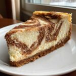 A close-up of a creamy slice of snickerdoodle cheesecake with a beautiful cinnamon swirl pattern on a white plate.