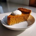 A close-up of a perfect slice of vegan pumpkin pie topped with a dollop of white whipped cream.