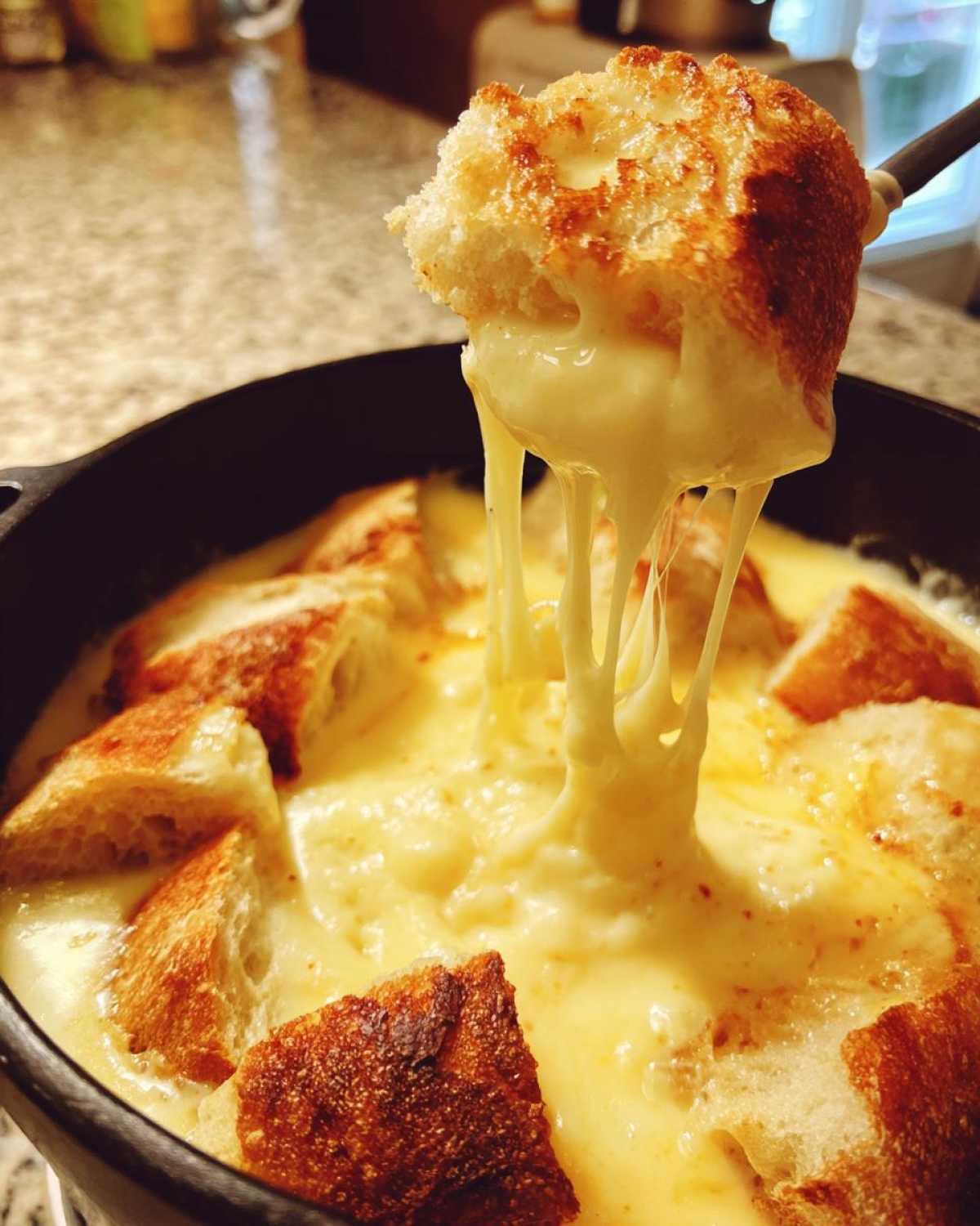 A piece of toasted bread being lifted from a pot of smooth, melted cheese fondue, showing long, stretchy cheese pulls.