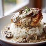 A perfectly seared chicken breast smothered in creamy mushroom sauce served over white rice, featuring the smothered chicken and rice.