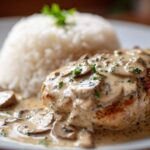 Close-up of smothered chicken and rice featuring a seared chicken breast covered in creamy mushroom sauce next to a mound of white rice.