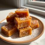 A stack of soft, square caramels generously topped with flaky sea salt, sitting on a small plate.