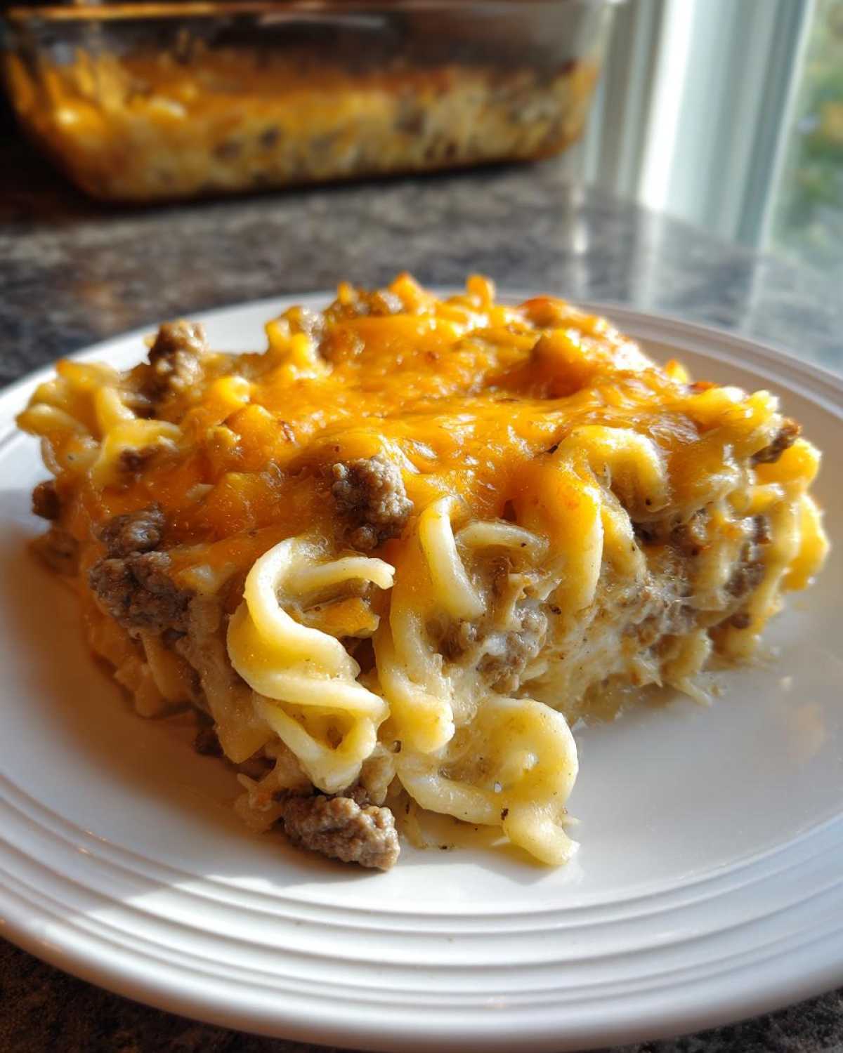 A close-up serving of sour cream beef noodle casserole topped with melted cheddar cheese on a white plate.