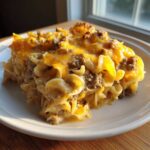 A close-up serving of creamy sour cream beef noodle casserole topped with melted cheddar cheese.