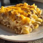 A generous serving of sour cream beef noodle casserole topped with melted cheddar cheese on a white plate.