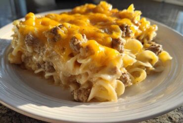 A generous serving of sour cream beef noodle casserole topped with melted cheddar cheese on a white plate.