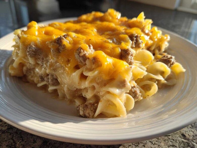 A generous serving of sour cream beef noodle casserole topped with melted cheddar cheese on a white plate.