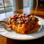 A close-up of a square serving of vibrant orange southern sweet potato casserole topped with crunchy pecans.