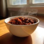 A steaming white bowl filled with rich, dark red chili, representing the best chili recipe.