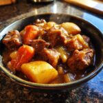 Close-up of a steaming bowl filled with rich, savory pork stew chunks, potatoes, and carrots in a thick sauce.