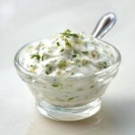 Close-up of rich, creamy tartar sauce recipe in a small glass bowl, garnished with fresh herbs.