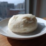 A smooth, round serving of white fufu dough placed on a white plate, ready to eat.