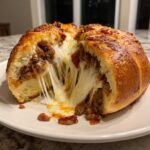 A cross-section of homemade garbage bread showing a massive, gooey cheese pull and savory meat filling.