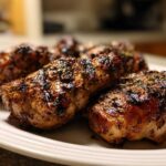 Close-up of perfectly grilled chicken pieces coated in a dark, glistening chicken marinade and sprinkled with herbs.