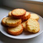A stack of golden-brown, round 3-ingredient butter cookies piled on a white plate.