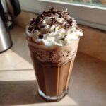 A tall glass filled with rich, blended frozen hot chocolate topped with whipped cream and chocolate shavings.