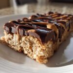 Close-up of a single slice of homemade protein bars topped with rich chocolate and peanut butter drizzle.