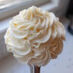 A close-up of beautifully piped, fluffy cream cheese frosting in a decorative swirl pattern.