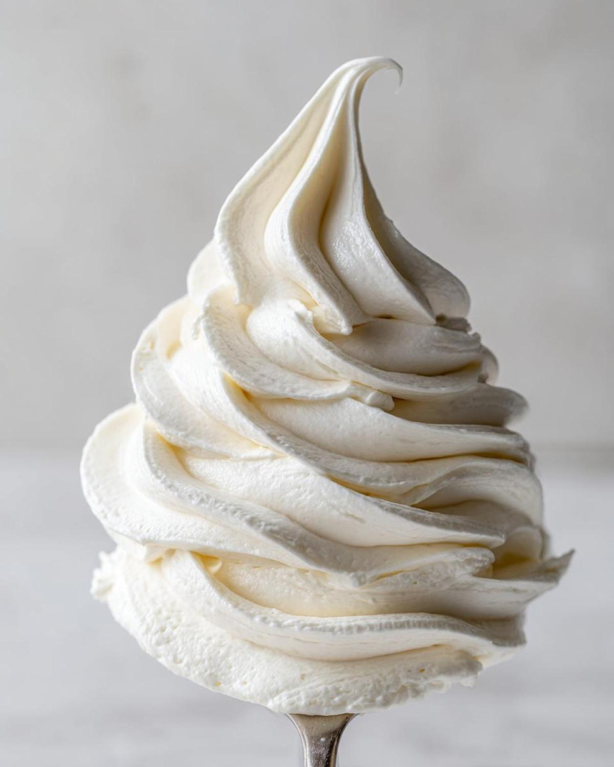 Close-up of a perfectly piped swirl of light, fluffy cream cheese frosting on a utensil.